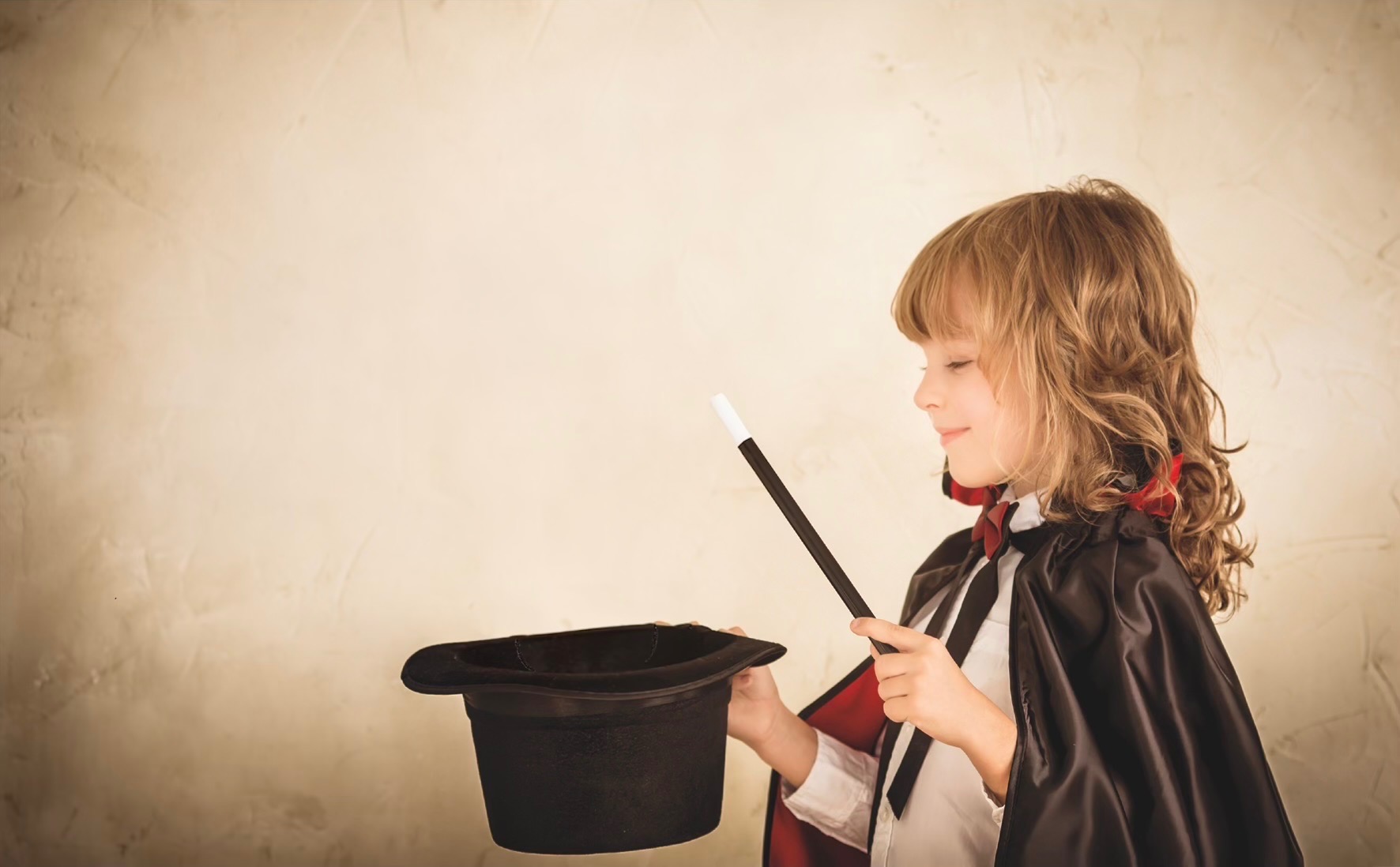 A young magician in a cape holding a wand over a top hat